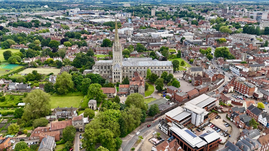 A vibrant public garden located near Reading town centre, featuring a well-maintained lawn with lush, trimmed grass and colorful flower beds filled with pink and red blossoms. The garden is bordered b
